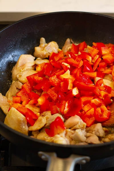 chicken and bell peppers being cooked in a wok.