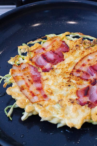 Okonomiyaki being cooked in a pan.