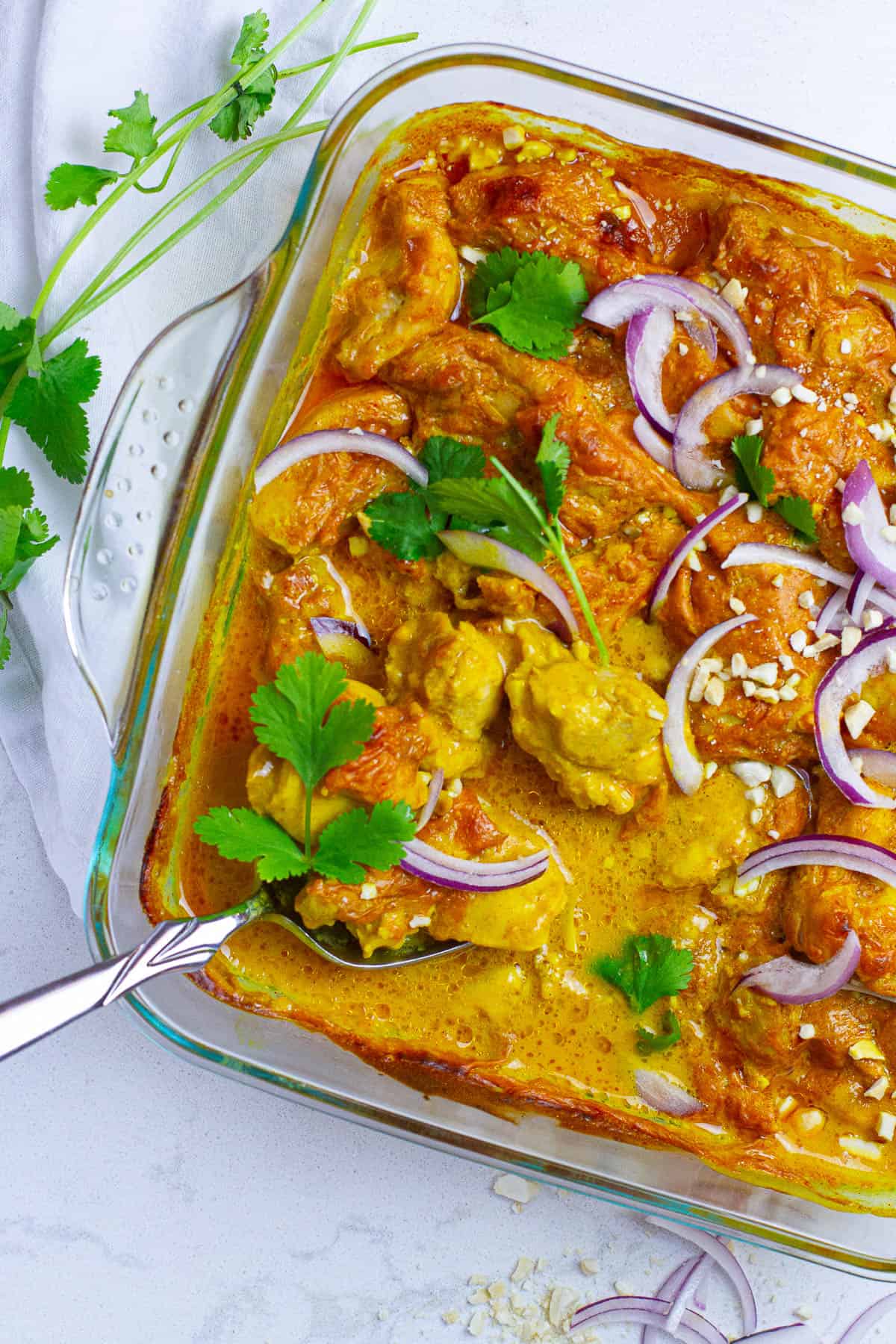 Baked curry chicken being scooped with a serving spoon.