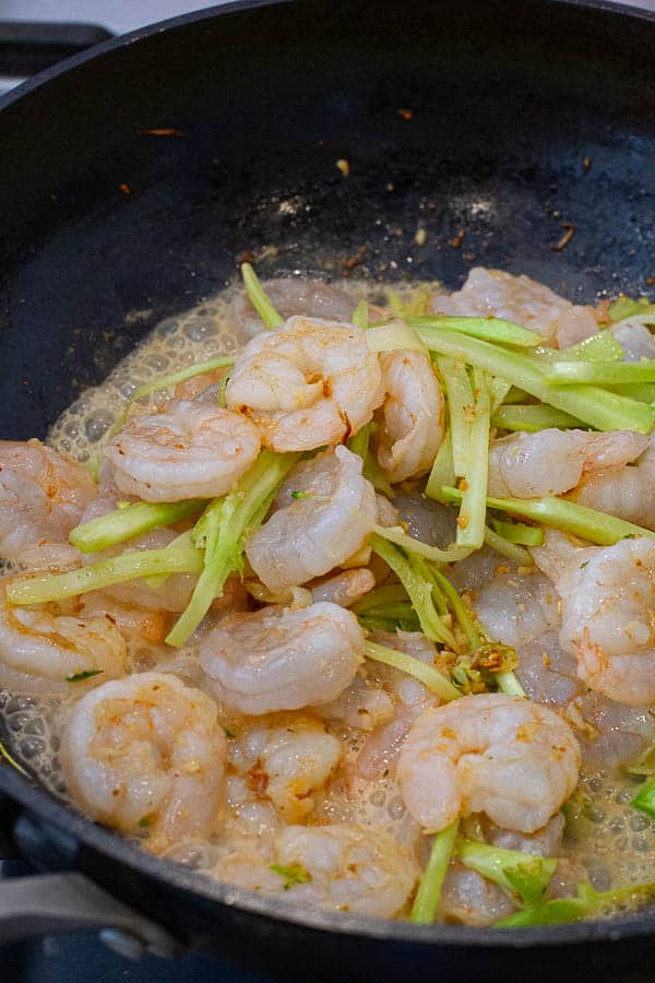 Broccoli stem and shrimp being cooked in a pan.