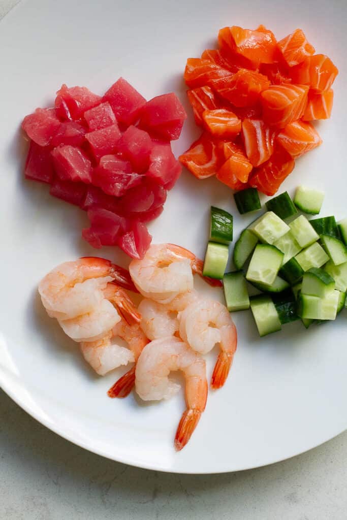 Cube tuna, salmon, cucumber, and shrimp on a plate.