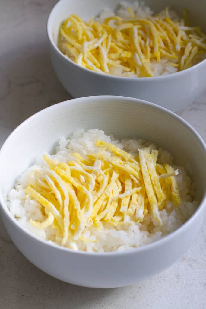 Two bowls of rice topped with egg threads.