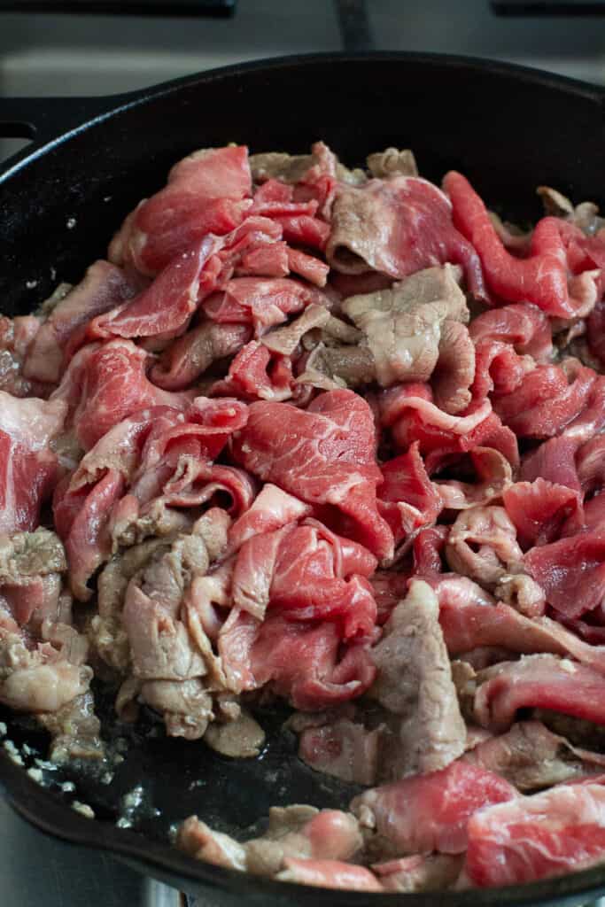 Thinly sliced beef being cooked in a skillet.