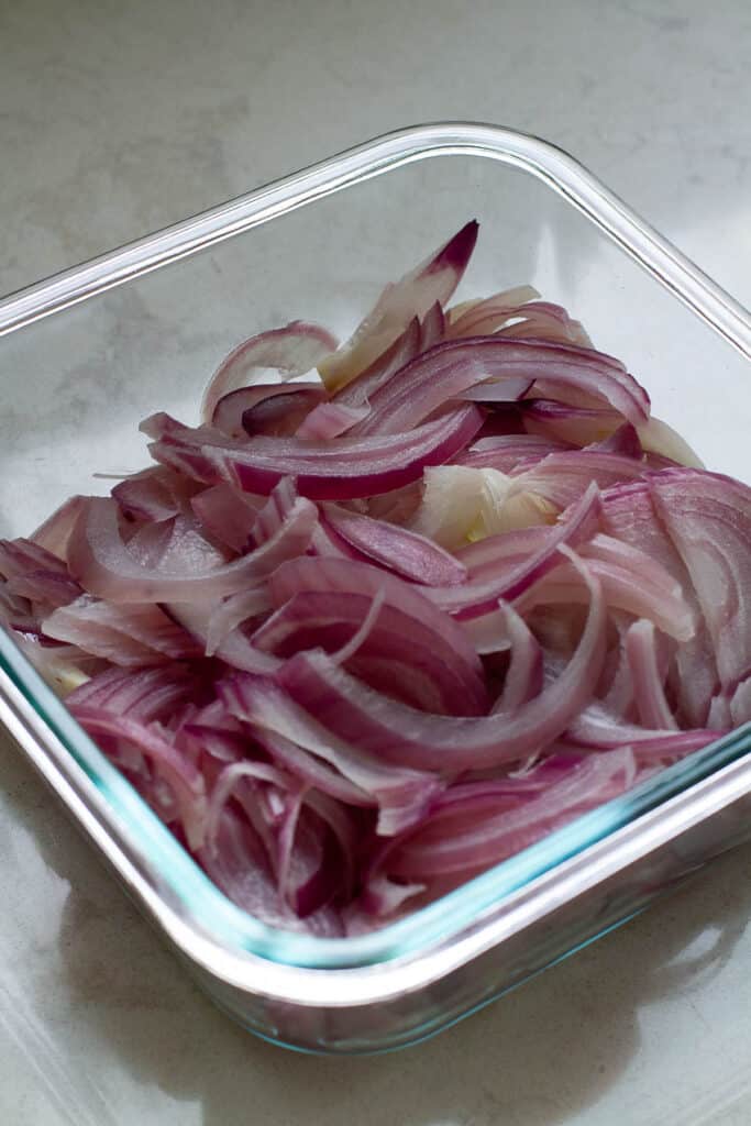 Lightly cooked red onions in a glass container.