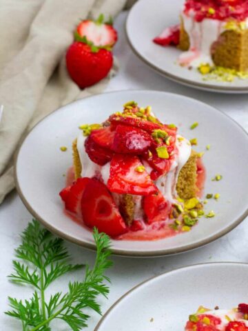 Strawberry snacking cake with coconut whipped cream and pistachio, served on a plate.
