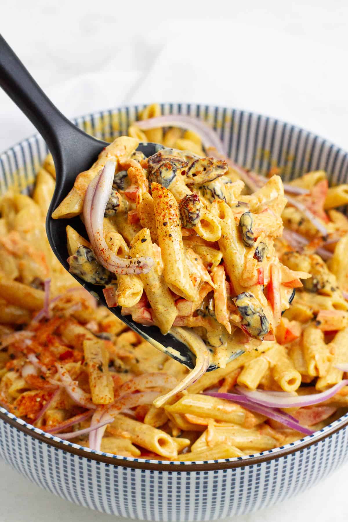 Red curry pasta salad being scooped with a ladle.