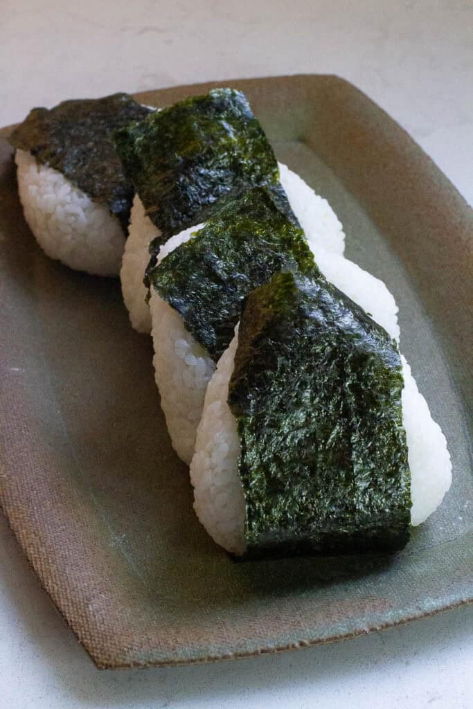 Four onigiri rice balls on a rectangular plate.