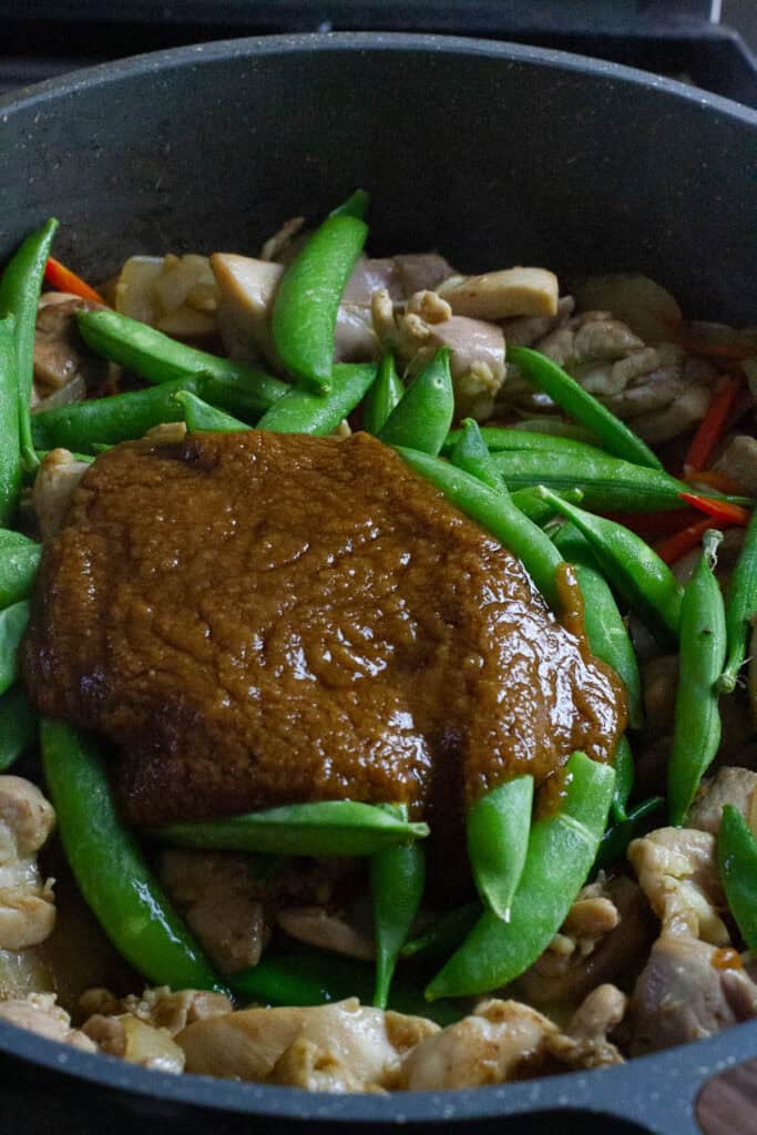 Vegetables, chicken thighs, and satay sauce in a skillet.