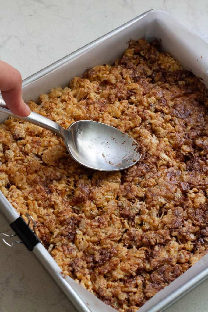 Chocolate peanut butter rice krispies being pressed down into a square pan.