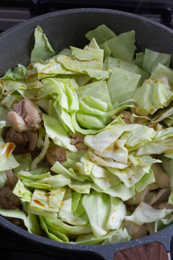 Cabbage and chicken being cooked in a pan.