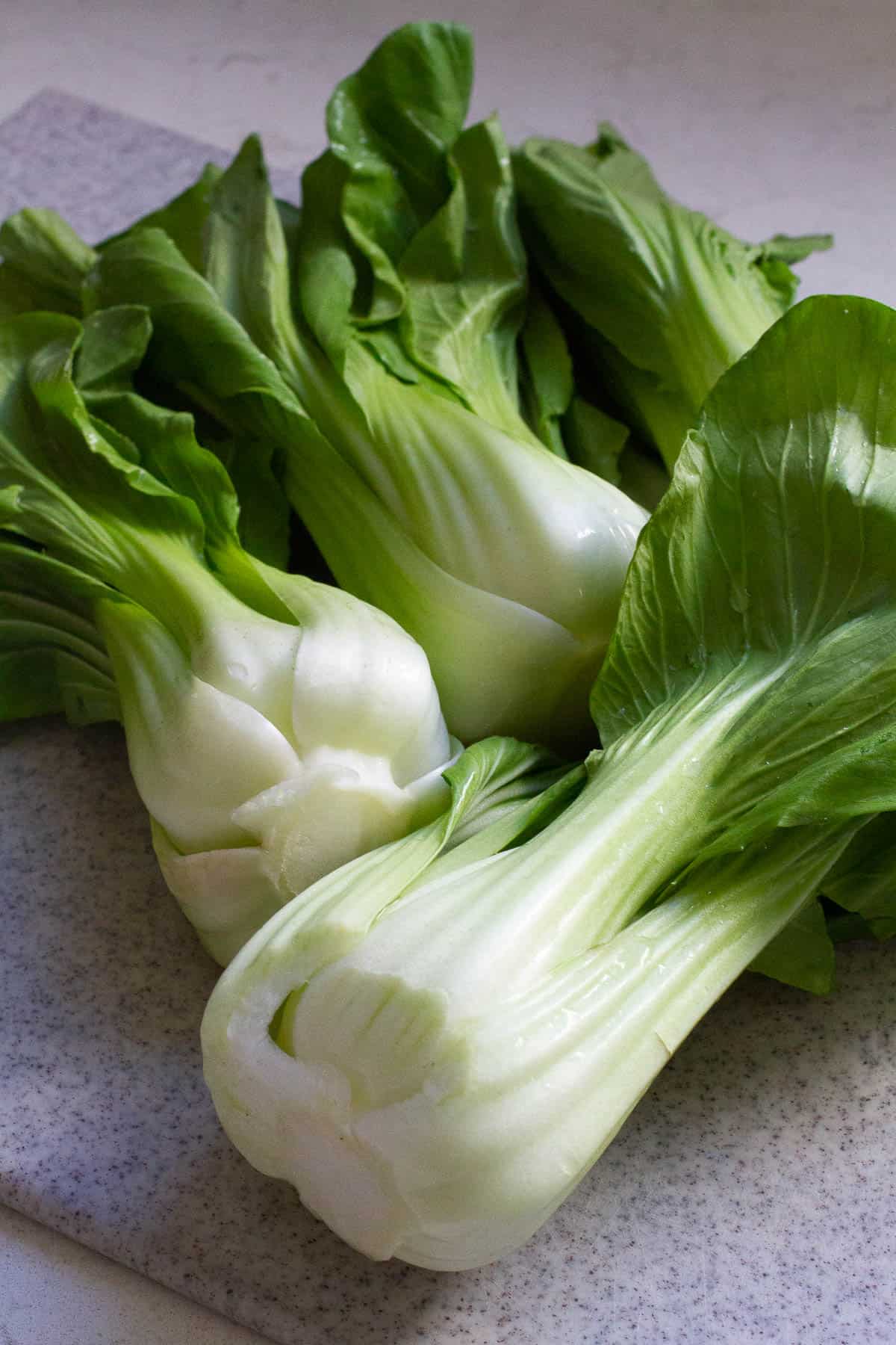 Uncooked baby bok choy on a cutting board.