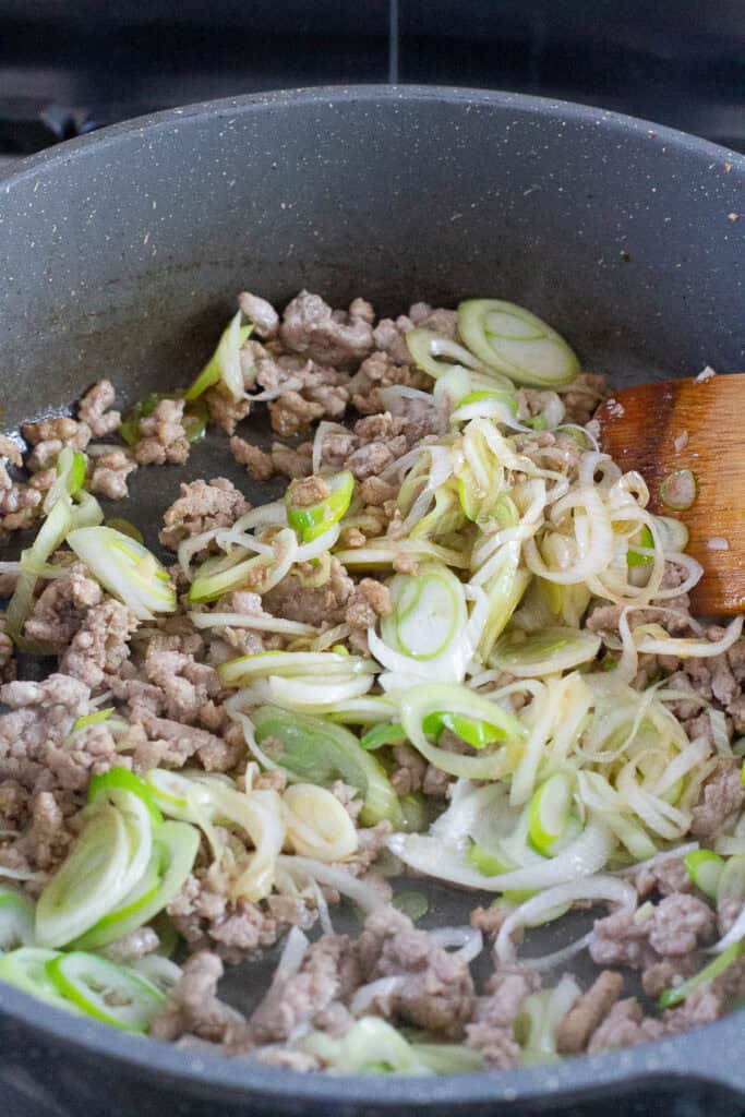 Ground pork and leek being cooked in a pan.