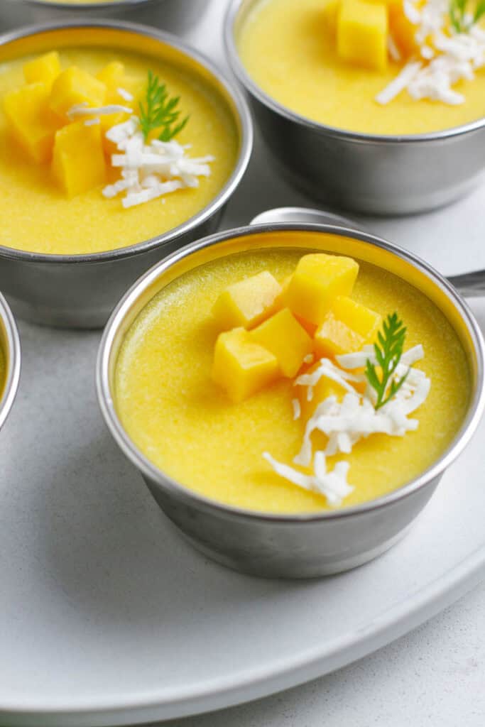 Close up shot of mango pudding with mango cubes and mint leave on top.