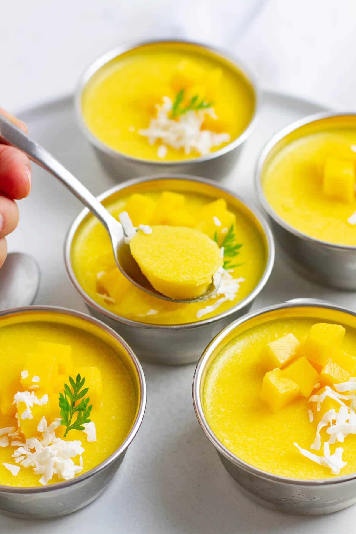 Mango pudding being scooped out of a cup with a spoon.