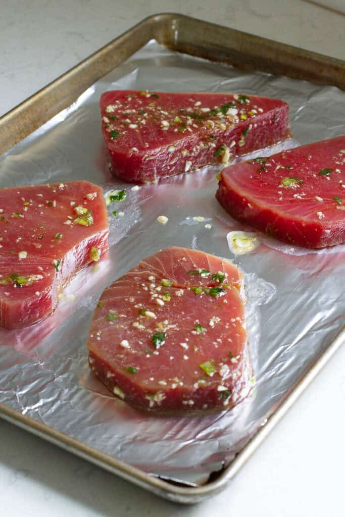 Marinated tuna steaks on a baking pan.
